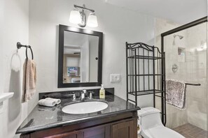 Un bagno con lavandino bianco, uno specchio, portasciuga e zona doccia.