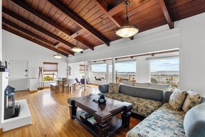 A spacious living area with a wooden ceiling, large windows offering a view of the city, and a cozy seating arrangement.