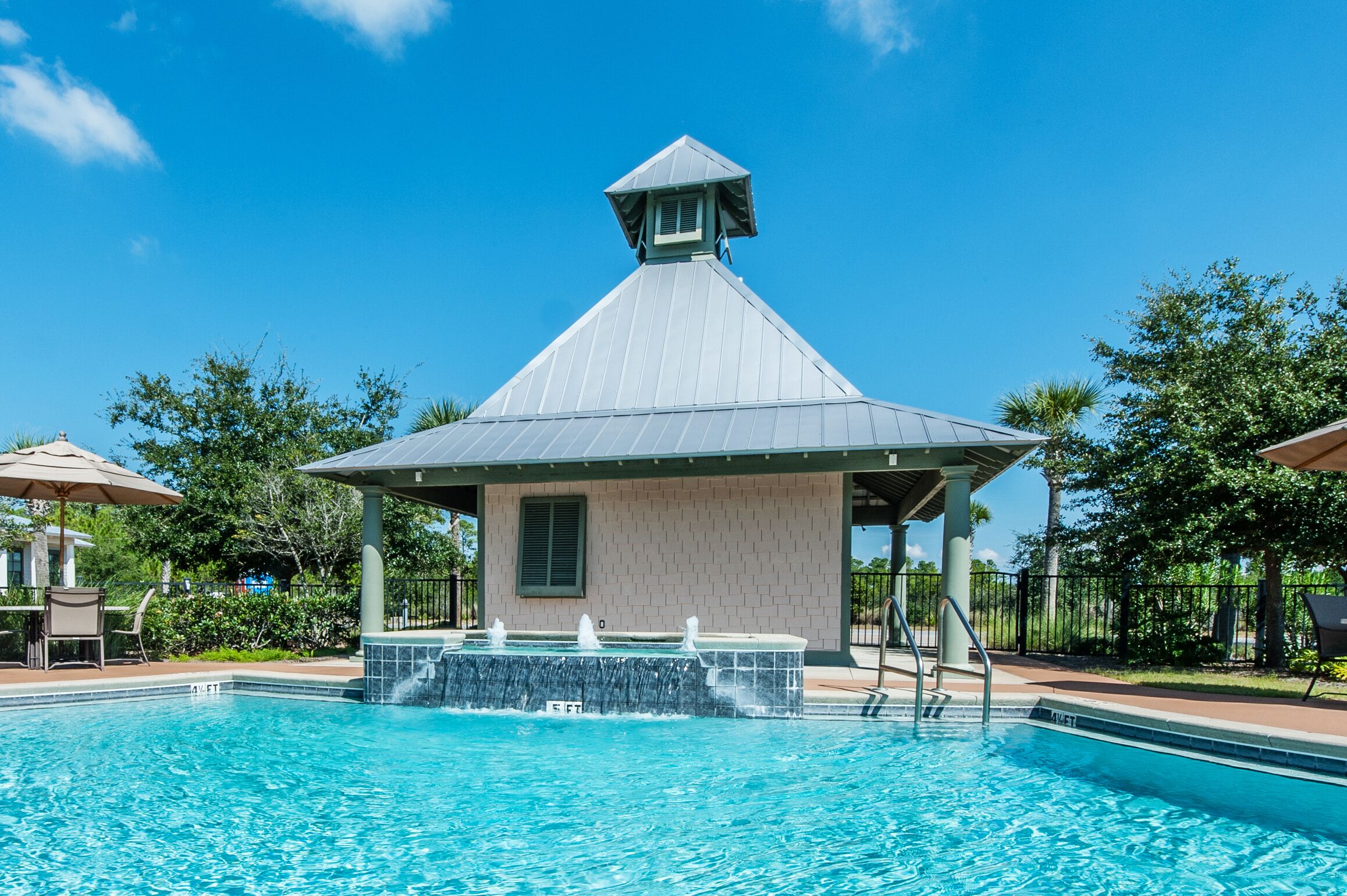 A swimming pool with a gazebo-like structure, surrounded by trees and outdoor seating.