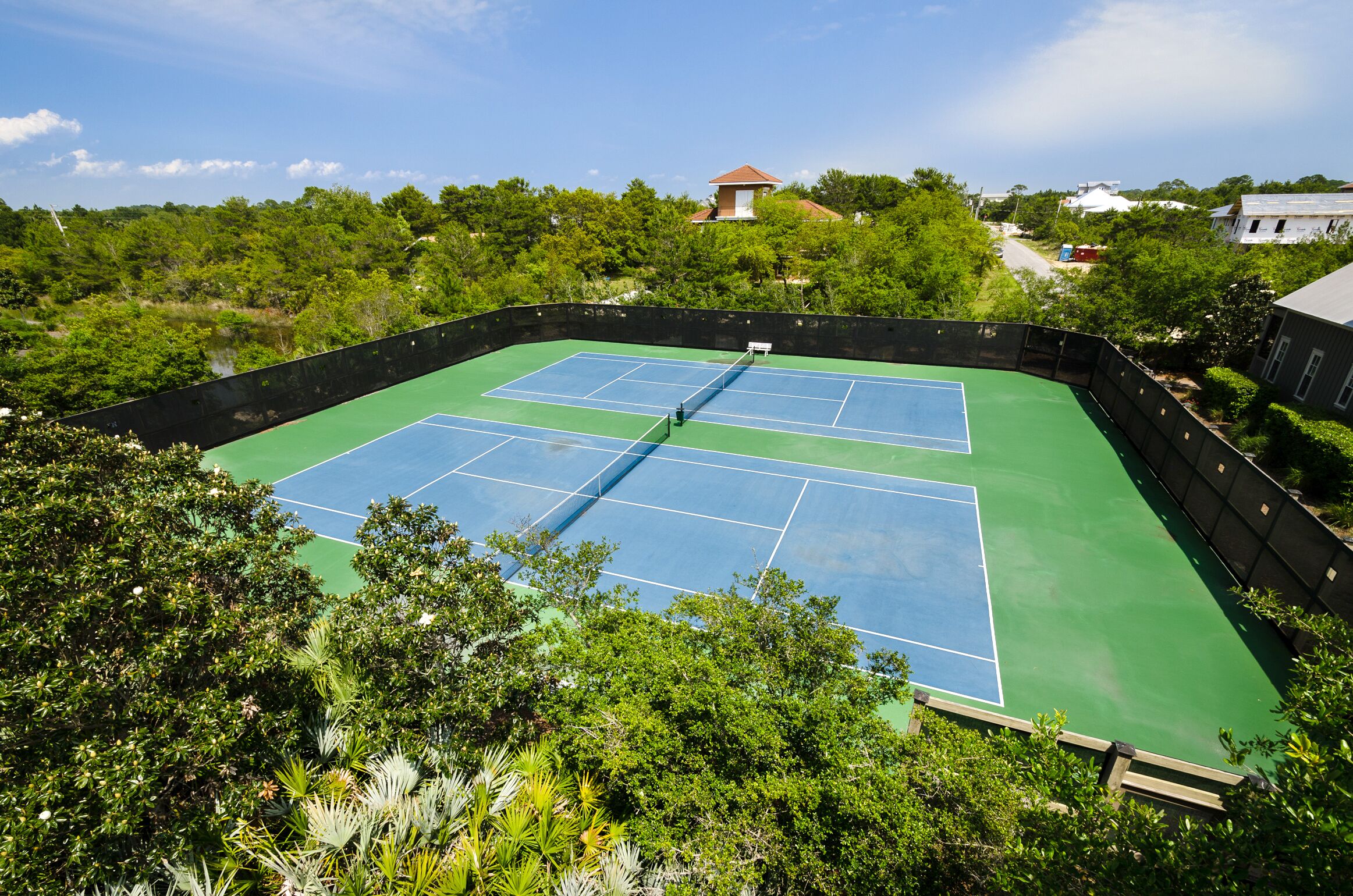Una cancha de tenis rodeada de exuberante vegetación y un cielo despejado.