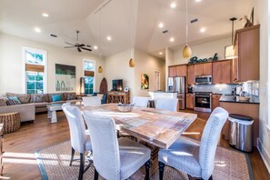 A spacious living area with a wooden dining table, light-colored chairs, and a modern kitchen with wooden cabinets and stainless steel appliances.
