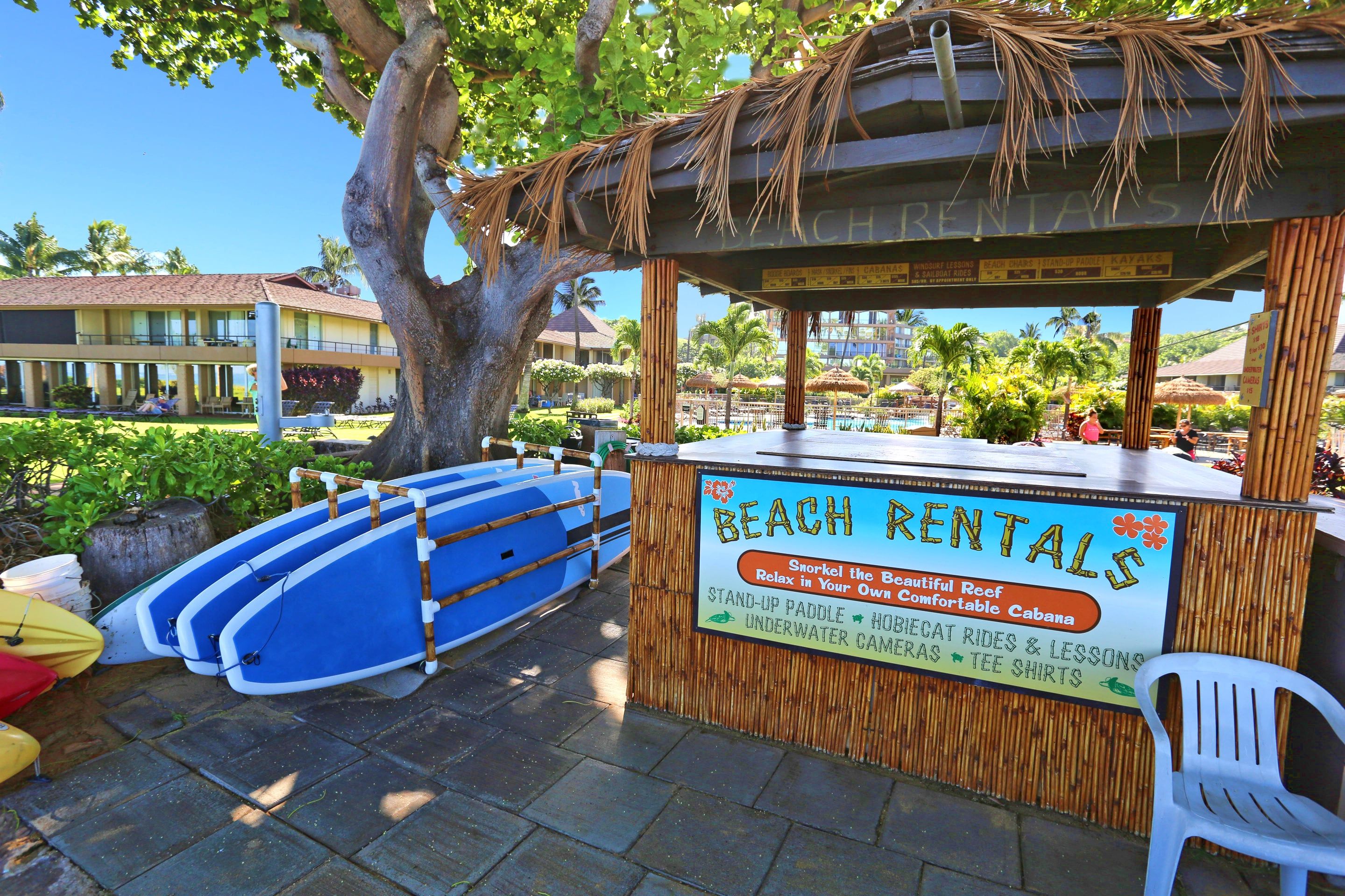 Un kiosque de location situé sur la plage, avec une enseigne publicitaire pour la location de planches de paddle, d’appareils photo sous-marins et de cabanes.