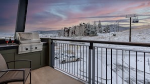 Ein Balkon mit Grill, einem Stuhl und Blick auf eine verschneite Landschaft mit einer Seilbahn.