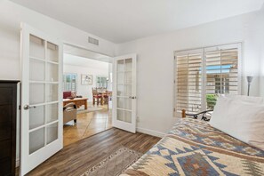Une chambre à coucher avec un lit, une fenêtre avec des stores et une porte donnant sur une autre pièce.