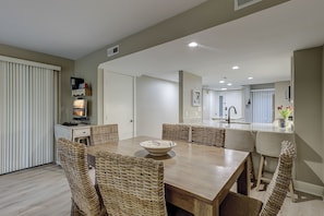 Uma cozinha moderna com uma ilha central, uma área de jantar com cadeiras de vime e vista para a sala de estar.