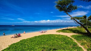 A beach with people sunbathing and a sailboat in the distance.