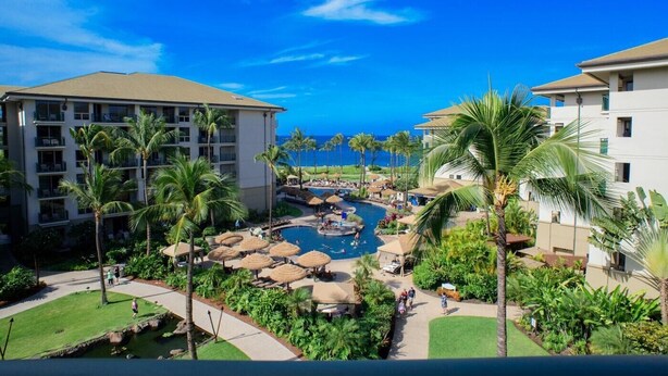 A resort with a pool area surrounded by palm trees and a view of the ocean.