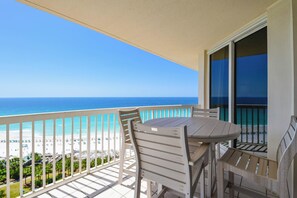 A balcony with a table and chairs, overlooking a beach with clear blue water and a sandy shore. - Cozy beachfront condo w/private balcony & elevator in Destin! ☀🌺🐚 (Destin)