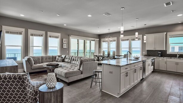 A spacious living area with a large sofa, a dining table, and a kitchen with white cabinets and a central island. - Luna Sol - Beachfront Duplex with Private Pool Area & Beach Access (Destin)