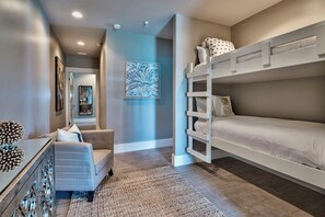 A bedroom with bunk beds, a sofa, a dresser, and artwork on the walls. - Luna Sol - Beachfront Duplex with Private Pool Area & Beach Access (Destin)