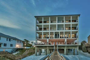 A multi-story beachfront building with balconies, a covered lower level, and a wooden staircase leading to the beach. - Luna Sol - Beachfront Duplex with Private Pool Area & Beach Access (Destin)