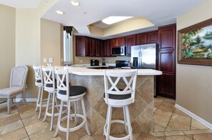 Una cocina con armarios de madera oscura, una isla central con taburetes de bar, un refrigerador y un microondas.