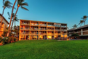 A multi-story hotel with balconies, a grassy lawn, and palm trees.