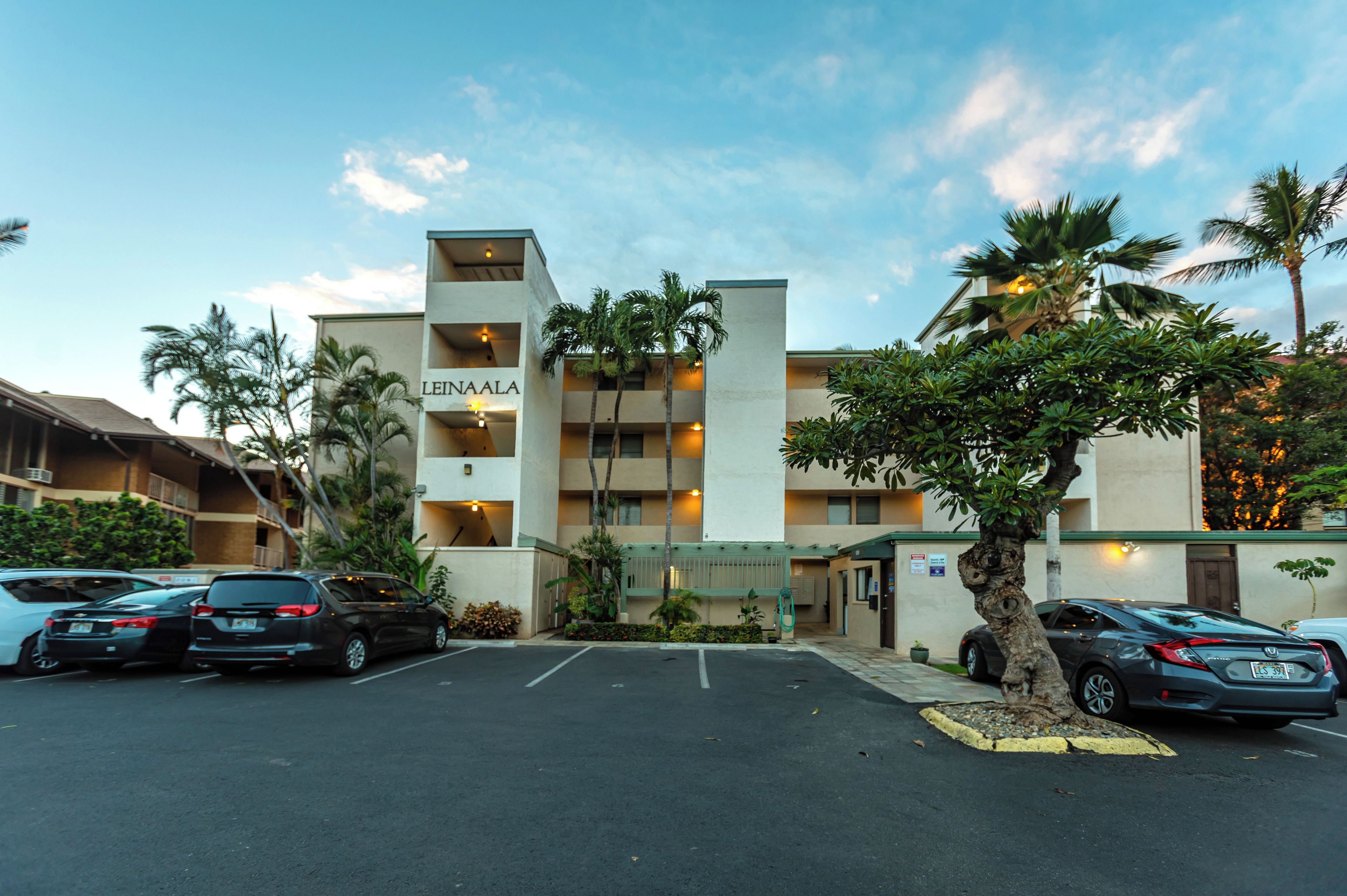 A hotel with a name sign, multiple floors, and a parking lot with cars.