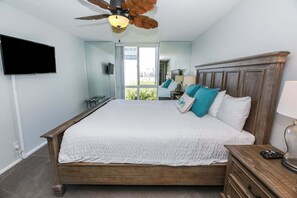 A bedroom with a bed, a ceiling fan, a television, and a view of the outdoors. - Modern Kitchen w/ Ocean & Harbor View- Upper Cottage, G32  North Coast Village (Oceanside)