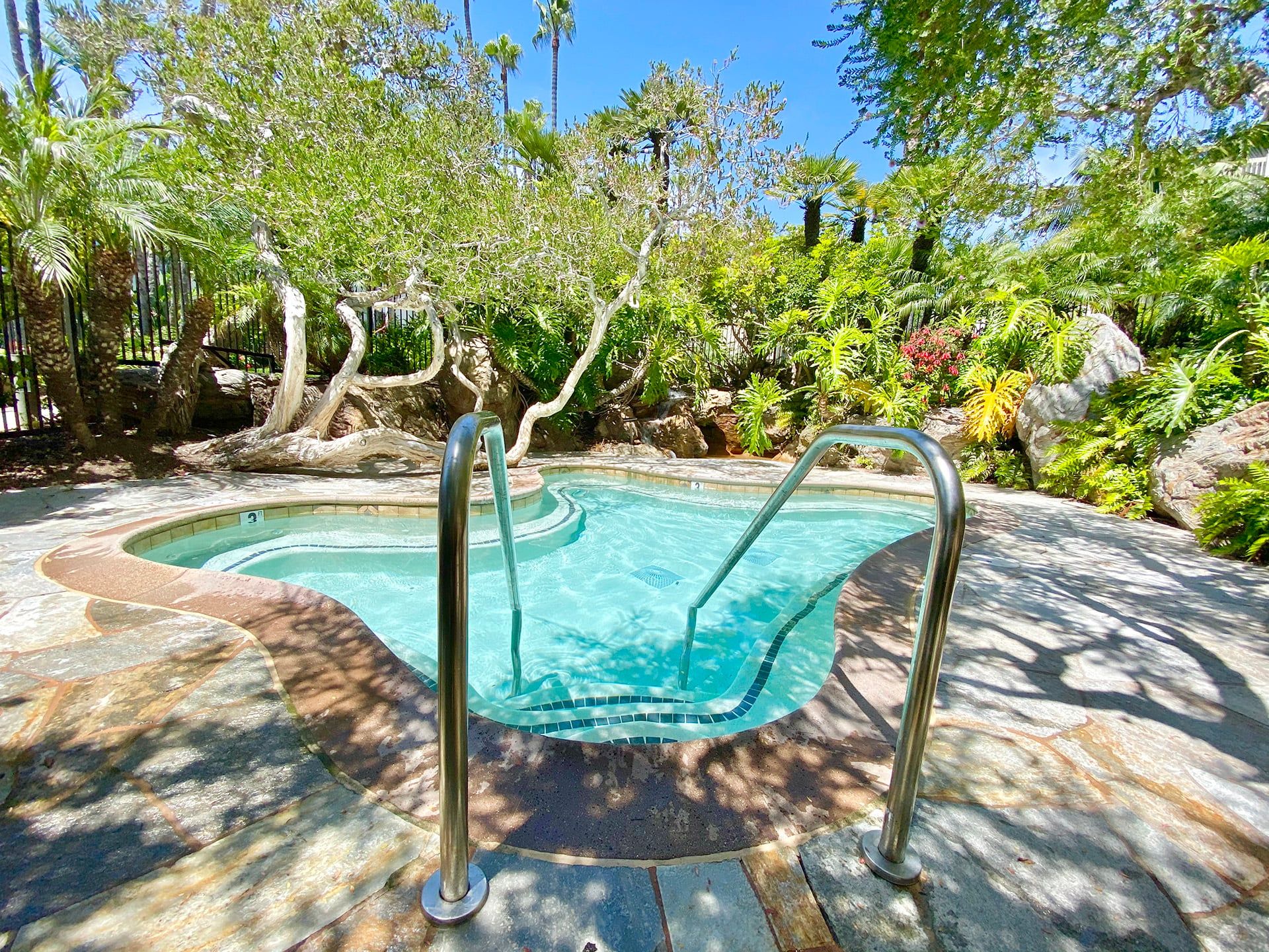 A swimming pool with a tiled edge, surrounded by a stone deck and lush greenery.