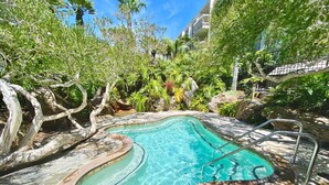 A swimming pool with a curved design, surrounded by lush greenery and a stone deck. - Modern Kitchen w/ Ocean & Harbor View- Upper Cottage, G32  North Coast Village (Oceanside)