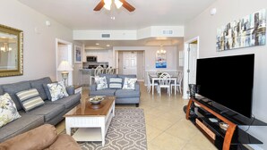 A spacious living room with a sofa, coffee table, TV, and a ceiling fan. - Fresh, fun, & bright beachfront condo w/private balcony! (Destin)