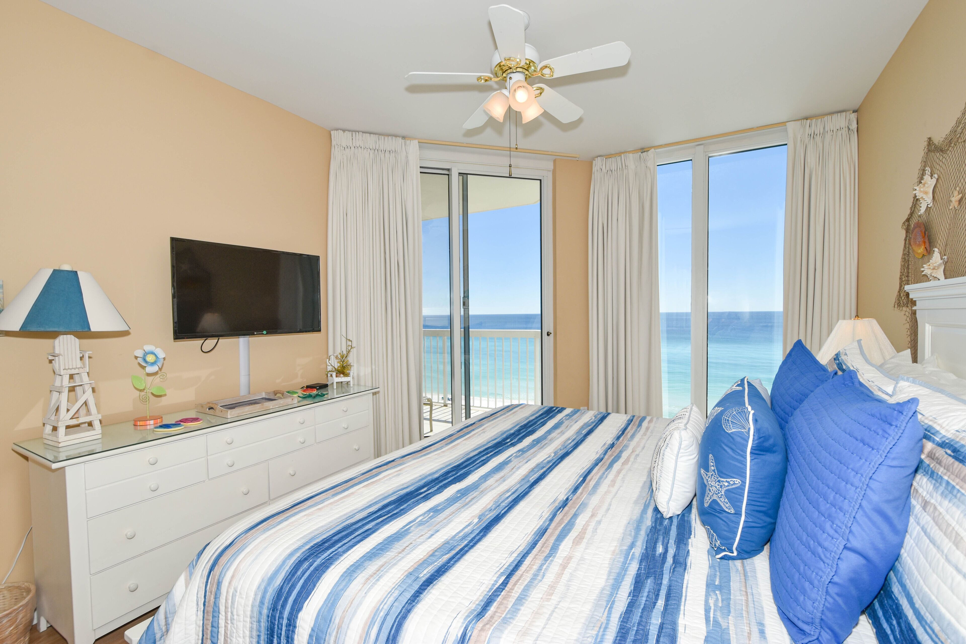 A bedroom with a bed, a TV, a dresser, and a view of the ocean.