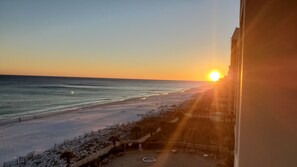 A beach view with a sunset, a fenced area with outdoor seating, and a pool. - Fresh, fun, & bright beachfront condo w/private balcony! (Destin)