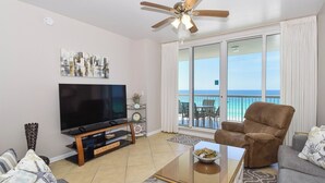 A living room with a flat-screen TV, a ceiling fan, a large window with a view of the ocean, and a brown recliner. - Fresh, fun, & bright beachfront condo w/private balcony! (Destin)