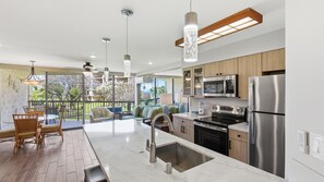 A modern kitchen with stainless steel appliances, a large island with a sink, and a dining area with wicker chairs.