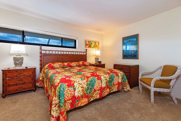 A bedroom with a wooden bed, a nightstand, a chair, a window, and a wall with a framed picture. - Oceanview Penthouse Condo - Spacious & Serene Sanctuary - Sugar Beach #PH12 (Kihei)