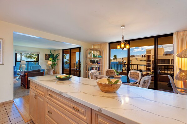 A modern kitchen with a marble countertop, wooden cabinets, and a view of the cityscape through large sliding doors.