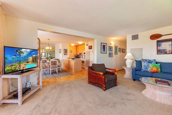 A living room with a television, a sofa, a chair, and a dining area with a kitchen in the background. - Oceanview Penthouse Condo - Spacious & Serene Sanctuary - Sugar Beach #PH12 (Kihei)