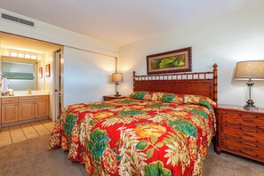 A bedroom with a large bed, a wooden nightstand, a bedside table, a mirror, and a framed picture on the wall.