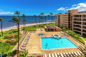 Ein Poolbereich eines Resorts mit Blick auf Strand und Meer, umgeben von Palmen und Liegestühlen.