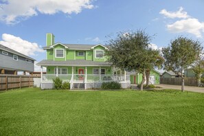 Une maison à deux étages, avec une façade verte, un porche à l’avant et une pelouse bien entretenue.