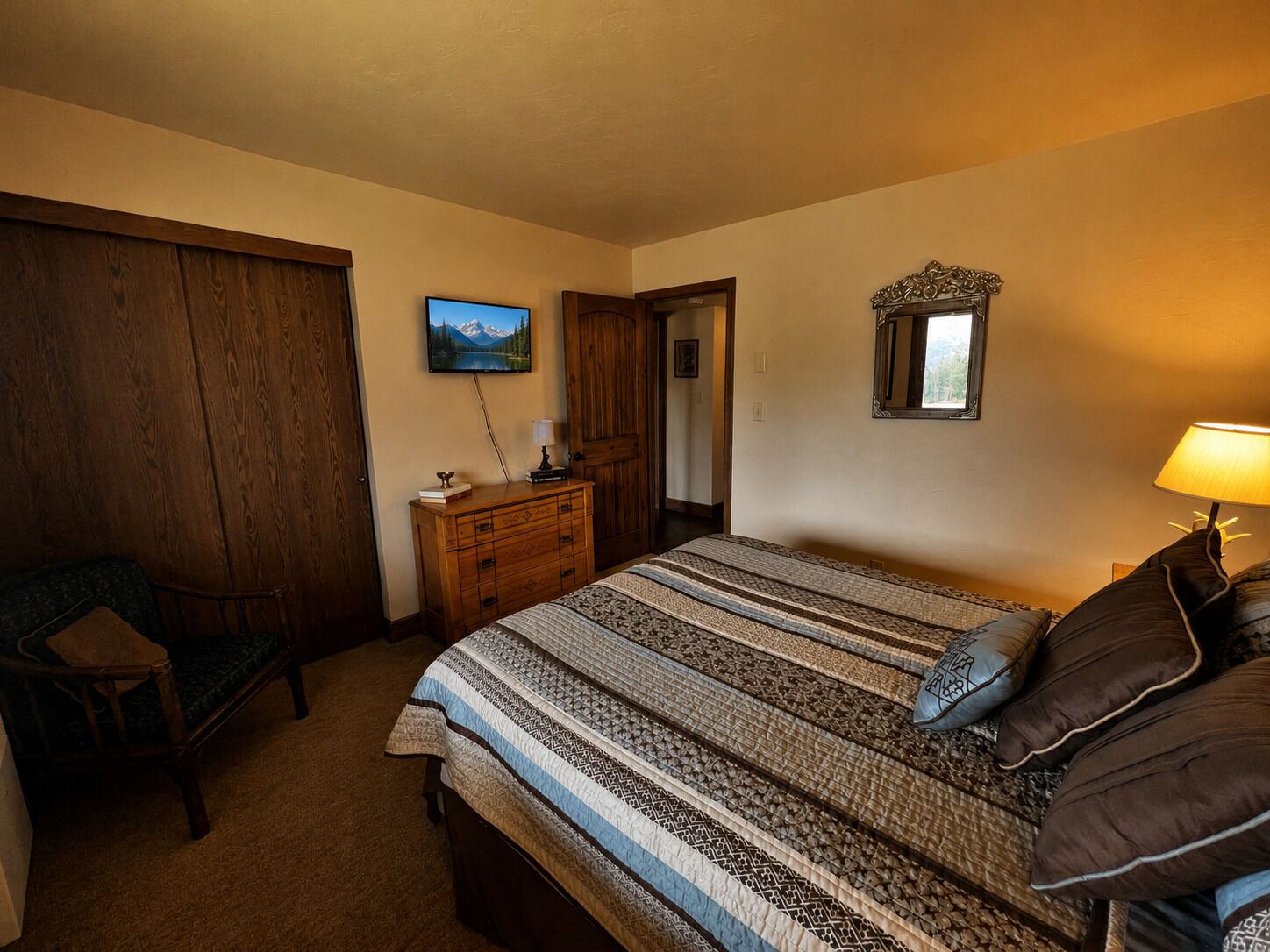 A bedroom with a bed, a dresser, a chair, a television, and a mirror.