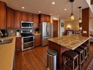 A modern kitchen with wooden cabinets, stainless steel appliances, a granite countertop, and a bar area.