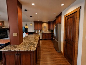 A modern kitchen with wooden cabinets, a granite countertop, stainless steel appliances, and pendant lighting.