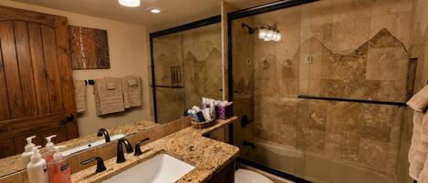 A bathroom with a granite countertop, a sink, a toilet, a shower with a glass door, and a mirror.
