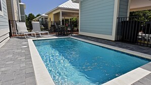 Una piscina con sillas de descanso y una mesa, rodeada por un patio de ladrillo y una valla de metal.