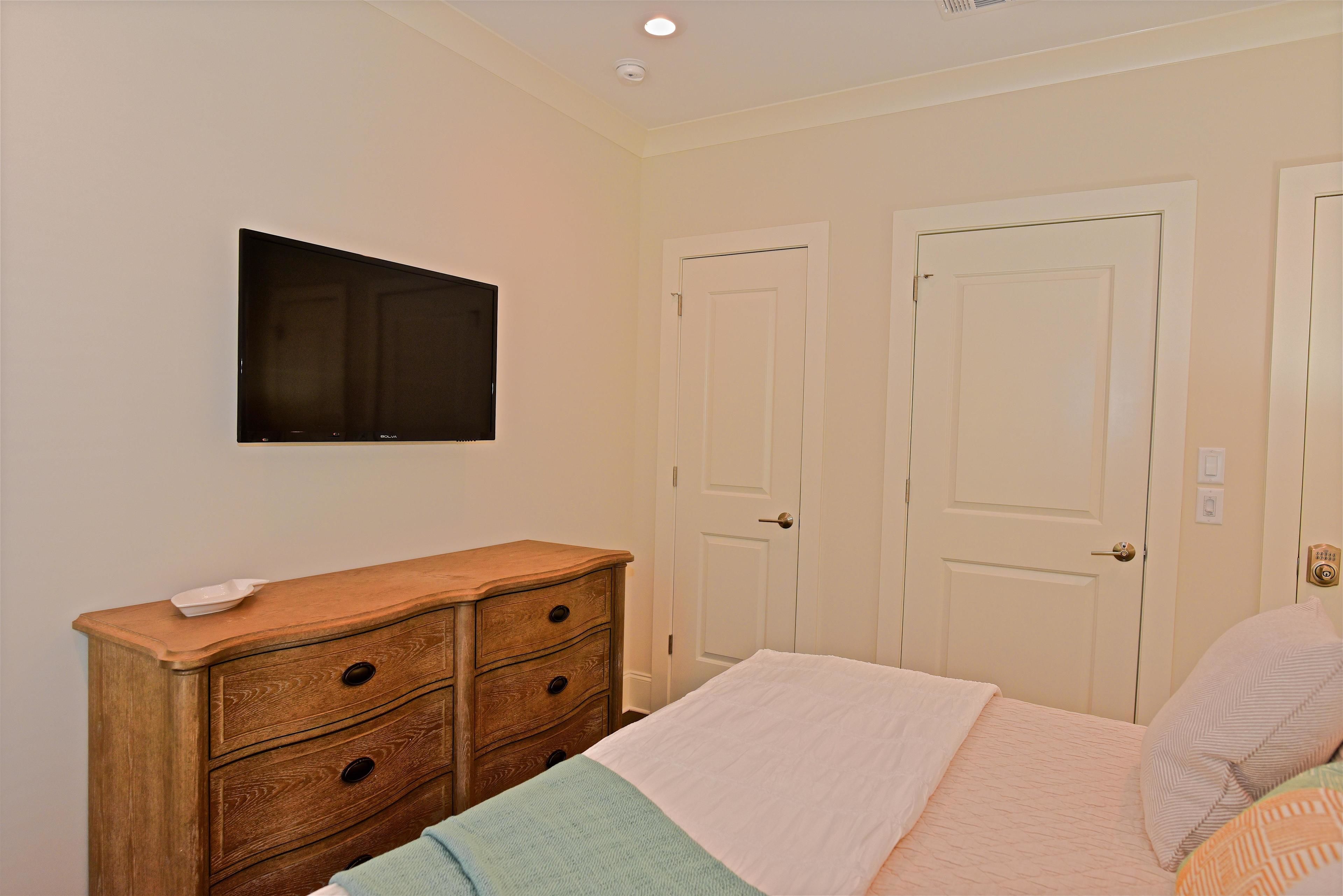 A bedroom with a bed, a dresser, a television, and two doors.
