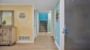 Un pasillo con piso de madera, una puerta con placa de número y una escalera que conduce a otra habitación.