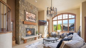 Un salón amplio con chimenea de piedra, asientos cómodos y ventanas grandes que ofrecen vistas al exterior.