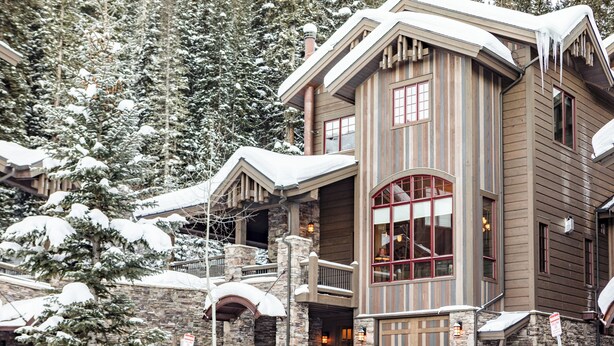 Un albergue de varios pisos con fachada de piedra, balcones de madera y un paisaje cubierto de nieve.