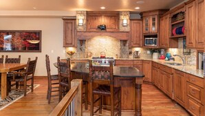 Una cocina con armarios de madera, una isla central con taburetes, un protector contra salpicaduras de piedra y un comedor con mesa y sillas.