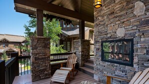 Terraza de madera con sillas Adirondack y un muro de piedra con una ventana.