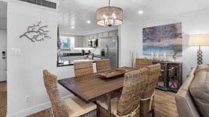 A modern kitchen with white cabinetry, a large island, and a dining area with wicker chairs and a wooden table.