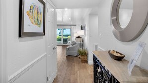 A hallway with a wooden floor, a framed artwork, a round mirror, and a view to a living area with a sofa and a lamp. - Beachfront, Large Pool, Convenient 1st Floor Unit, + Free Attraction Tickets! (Seacrest)