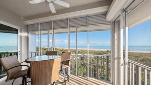 A balcony with a table and chairs, overlooking a beach and ocean. - Beachfront Bliss at Shell Island Beach Club 5D (Sanibel Island)