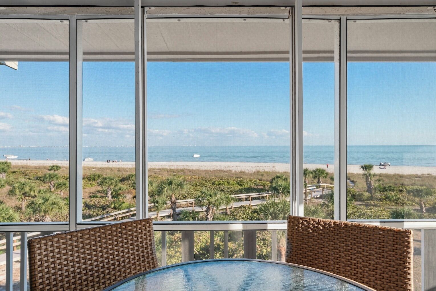 A beach view from a covered patio with wicker furniture.