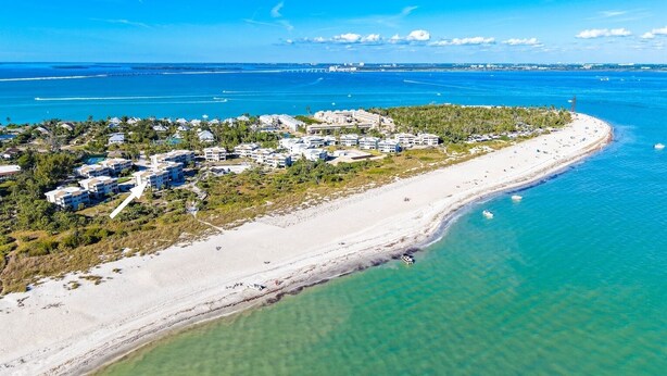 An aerial view of a coastal resort with beachfront properties, clear blue waters, and a distant pier. - Beachfront Bliss at Shell Island Beach Club 5D (Sanibel Island)