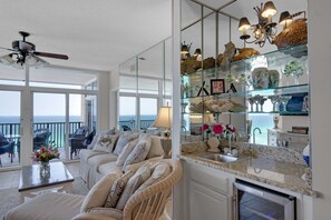 A spacious living room with a balcony, a glass display cabinet with decorative items, and a modern kitchen with a built-in dishwasher. - BEACH FRONT W/ PRIVATE BALCONY!! ELEGANT UNIT THAT SLEEPS 8! (Destin)