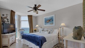 Un dormitorio con cama, televisión, ventilador de techo, ventana con cortinas, un cuadro de tortuga y una escultura decorativa de pez.